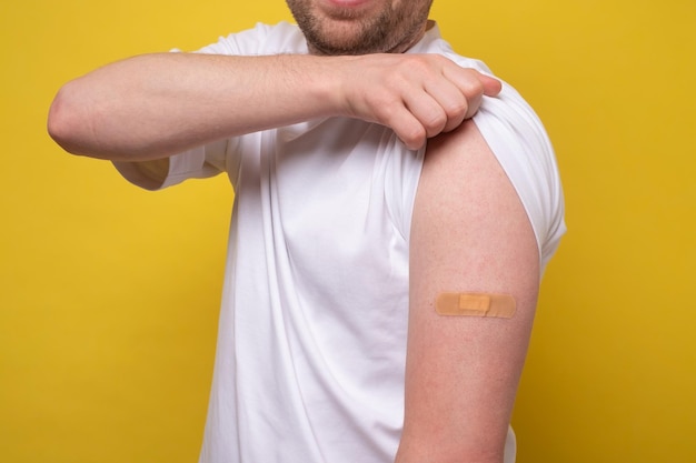 Caucasian man showing his vaccinated arm He received a corona vaccine looking at camera Studio shot on yellow wall