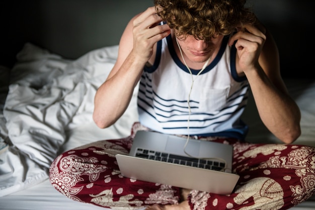 Photo a caucasian man sitting on the bed using a laptop