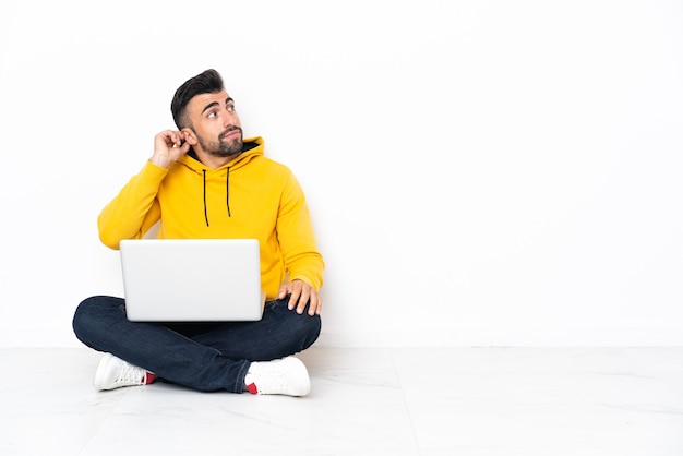 Caucasian man sitting on the floor with his laptop thinking an idea