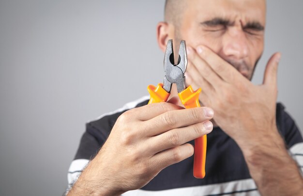 Caucasian man suffering from toothache holding pliers.