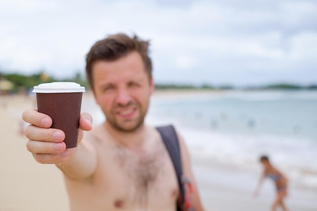 Caucasian man on summer beach suggesting cup of coffee