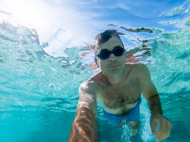 Caucasian man swimming under the water in swimming goggles  blue transparent water