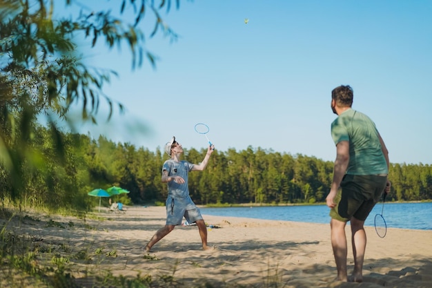 Caucasian man and teenager son playing badminton on the lakeside Parents and teens concept Image with selective focus