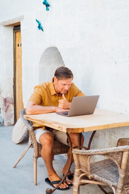 Caucasian man using laptop outside sitting at wooden table in hotel people working on vacation