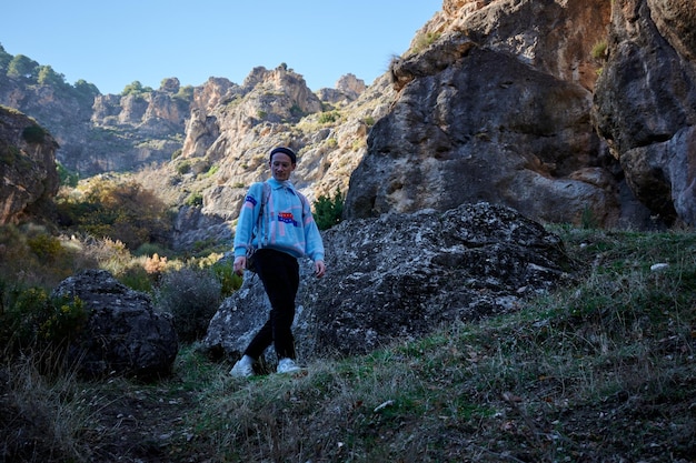 A caucasian man walking in a canyon with high rocky mountains in the background