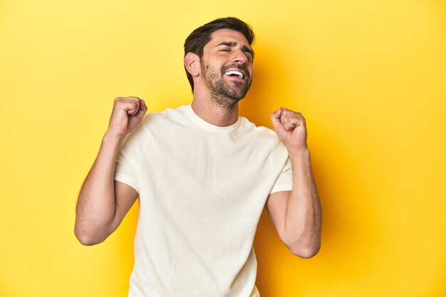 Photo caucasian man in white tshirt on yellow studio background celebrating a victory passion