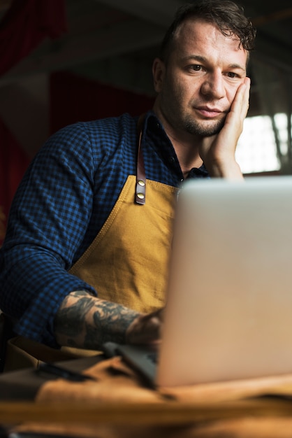 Caucasian man with apron using computer laptop thoughtful