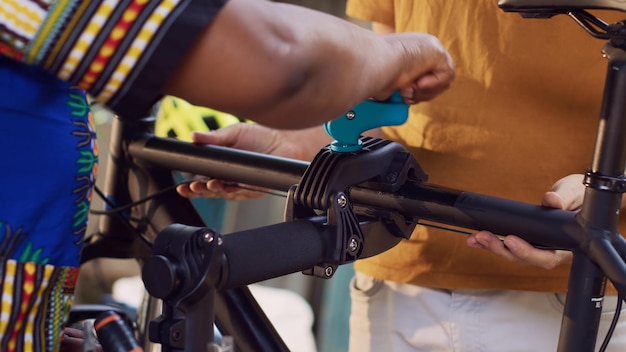 Caucasian man with assistance from black woman are carefully placing bicycle to repair-stand for further maintenance and repair. Outdoor summer bike adjustment, couples hobby activity.