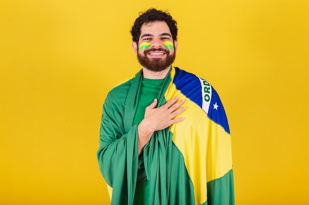 Caucasian man with beard brazilian soccer fan from brazil\
singing national anthem with hand on chest