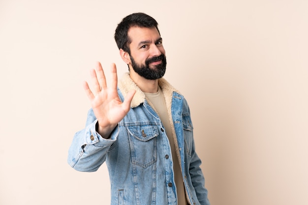 Кавказский мужчина с бородой над изолированной стеной считает пять пальцами