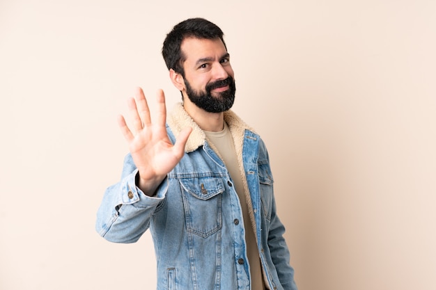 Uomo caucasico con la barba sopra la parete isolata che conta cinque con le dita