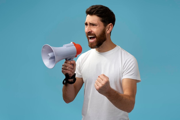 Caucasian man with beard loudly screaming at bullhorn megaphone and looking at distance