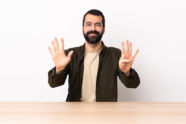 Caucasian man with beard in a table counting nine with fingers.