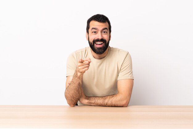 Caucasian man with beard in a table surprised and pointing front