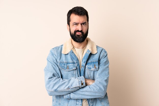 Caucasian man with beard over wall with unhappy expression