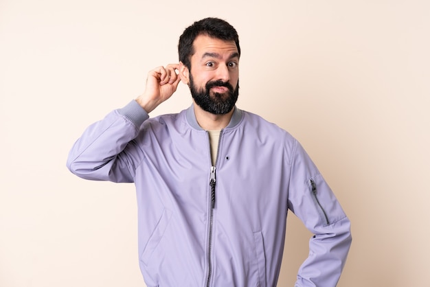 Caucasian man with beard wearing a jacket over isolated background having doubts