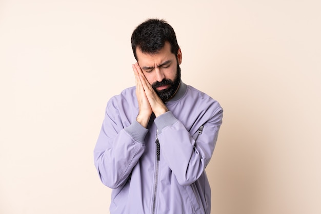 Caucasian man with beard wearing a jacket over isolated background making sleep gesture in dorable expression