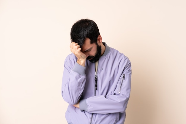 Caucasian man with beard wearing a jacket over isolated wall with headache