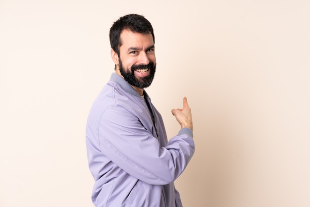 Caucasian man with beard wearing a jacket pointing back