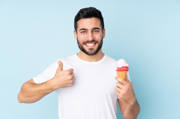 Uomo caucasico con un gelato di cornetta sulla parete blu con il pollice in alto perché è successo qualcosa di buono