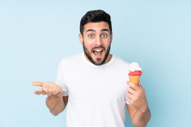 Caucasian man with a cornet ice cream isolated on blue wall with shocked facial expression