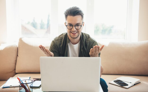 L'uomo caucasico con gli occhiali sta tenendo una lezione online a casa utilizzando un laptop e sta spiegando qualcosa