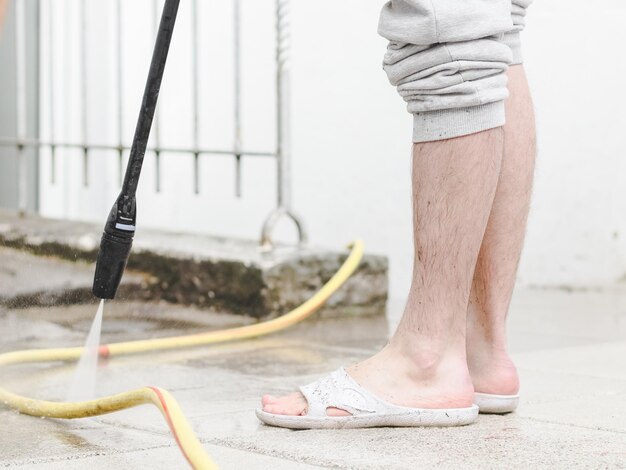 A caucasian man with hairy legs in white slippers washes the stone tiles of the terrace