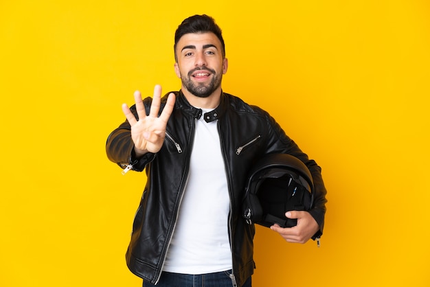 Кавказский человек в мотоциклетном шлеме над желтым счастливым и считает четыре пальцами