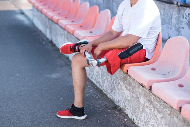 Caucasian man with a prosthesis on his leg close up sitting on\
a bench.