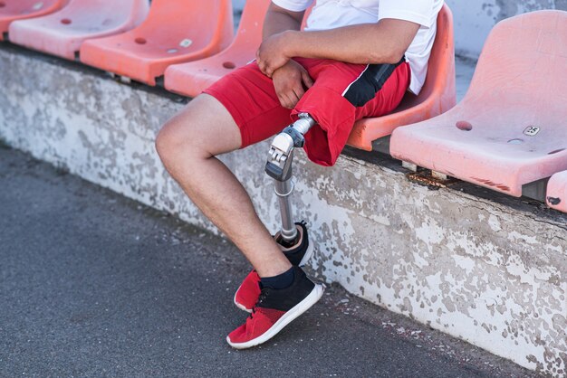 Caucasian man with a prosthesis on his leg close up sitting on\
a bench.