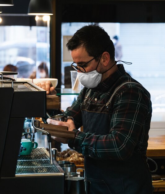 Caucasian masked barista heating milk in the coffee machine