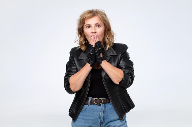 Caucasian mature lady in leather jacket covering her mouth with palms