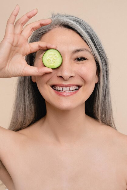 Caucasian mature middleaged woman with grey hair and soft clear\
aging skin holding cucumber