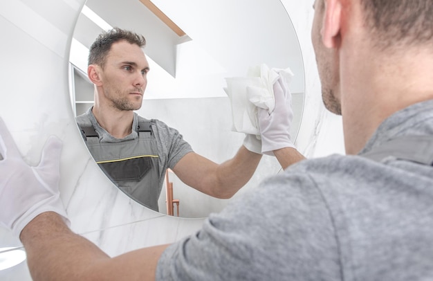 Caucasian men cleaning circular bathroom mirror using paper towel finishing newly remodeled bathroom