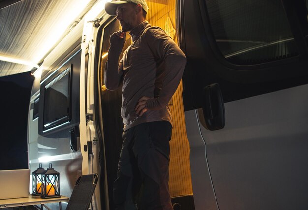 Photo caucasian men in front of his class b camper van with extended awning summer evening in a rv park campsite