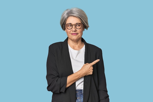 Caucasian midage female in business suit smiling and pointing aside showing something at blank space