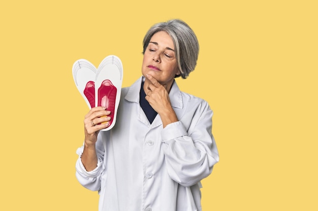 Photo caucasian midage female podiatrist holding insole looking sideways with doubtful and skeptical expression