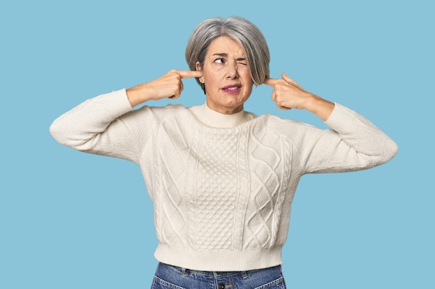 Photo caucasian midage female on studio background covering ears with fingers stressed and desperate by a loudly ambient