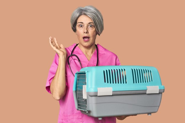 Caucasian midage vet holding pet carrier surprised and shocked