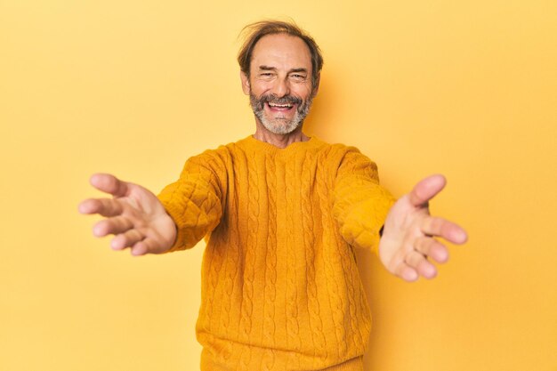 Caucasian middleaged man in yellow studio feels confident giving a hug to the camera