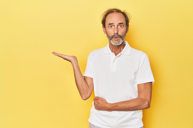 Caucasian middleaged man in yellow studio impressed holding copy space on palm