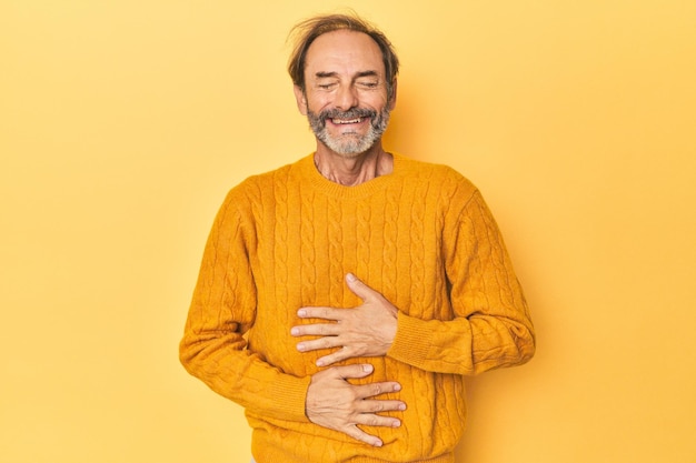 Caucasian middleaged man in yellow studio laughs happily and has fun keeping hands on stomach