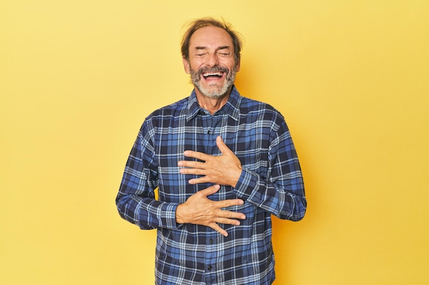 Foto un uomo caucasico di mezza età in studio giallo ride felice e si diverte a tenere le mani sullo stomaco