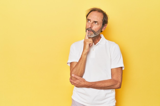Caucasian middleaged man in yellow studio looking sideways with doubtful and skeptical expression