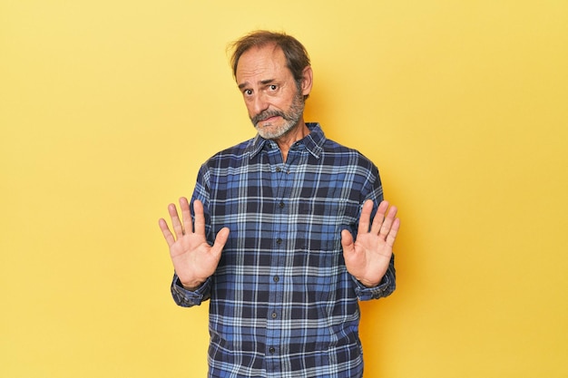 Caucasian middleaged man in yellow studio rejecting someone showing a gesture of disgust