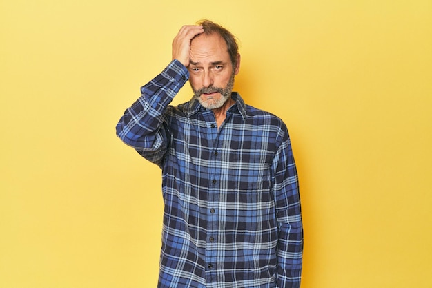 Caucasian middleaged man in yellow studio tired and very sleepy keeping hand on head