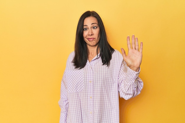 Caucasian middleaged woman against yellow backdrop smiling cheerful showing number five with fingers