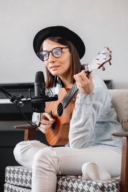 Donna caucasica millenaria in un cappello con un microfono, suonare la chitarra o l'ukulele