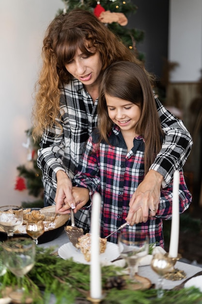 Foto la mamma e la figlia caucasiche tagliano la torta di mele di natale e la mettono sui piatti su un tavolo festivo decorato con candele per cena