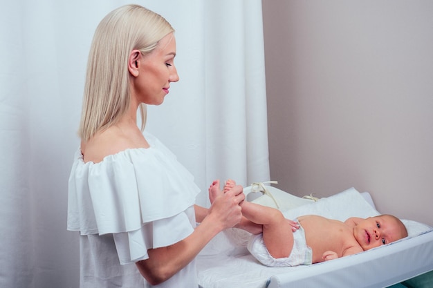 Caucasian mother applying baby powder before putting diapers on her four month old baby in bed at home on the changing table